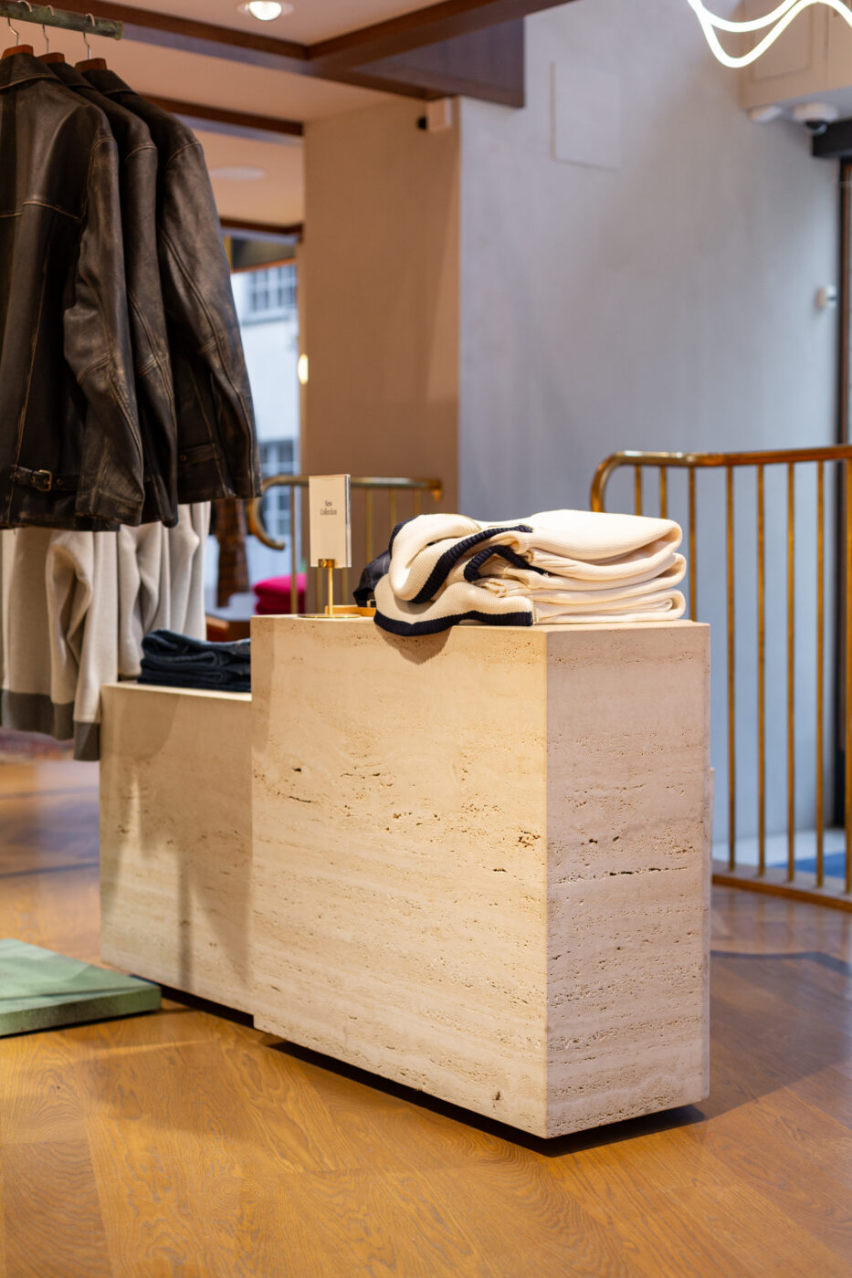 Gant Store interjöör beegi kiviplokkidega tahvel, sinakas-valged s’obritud sallid ja valged kudumid ning mustad nahkjacketsid, avatud ruum ja puidust põrand.