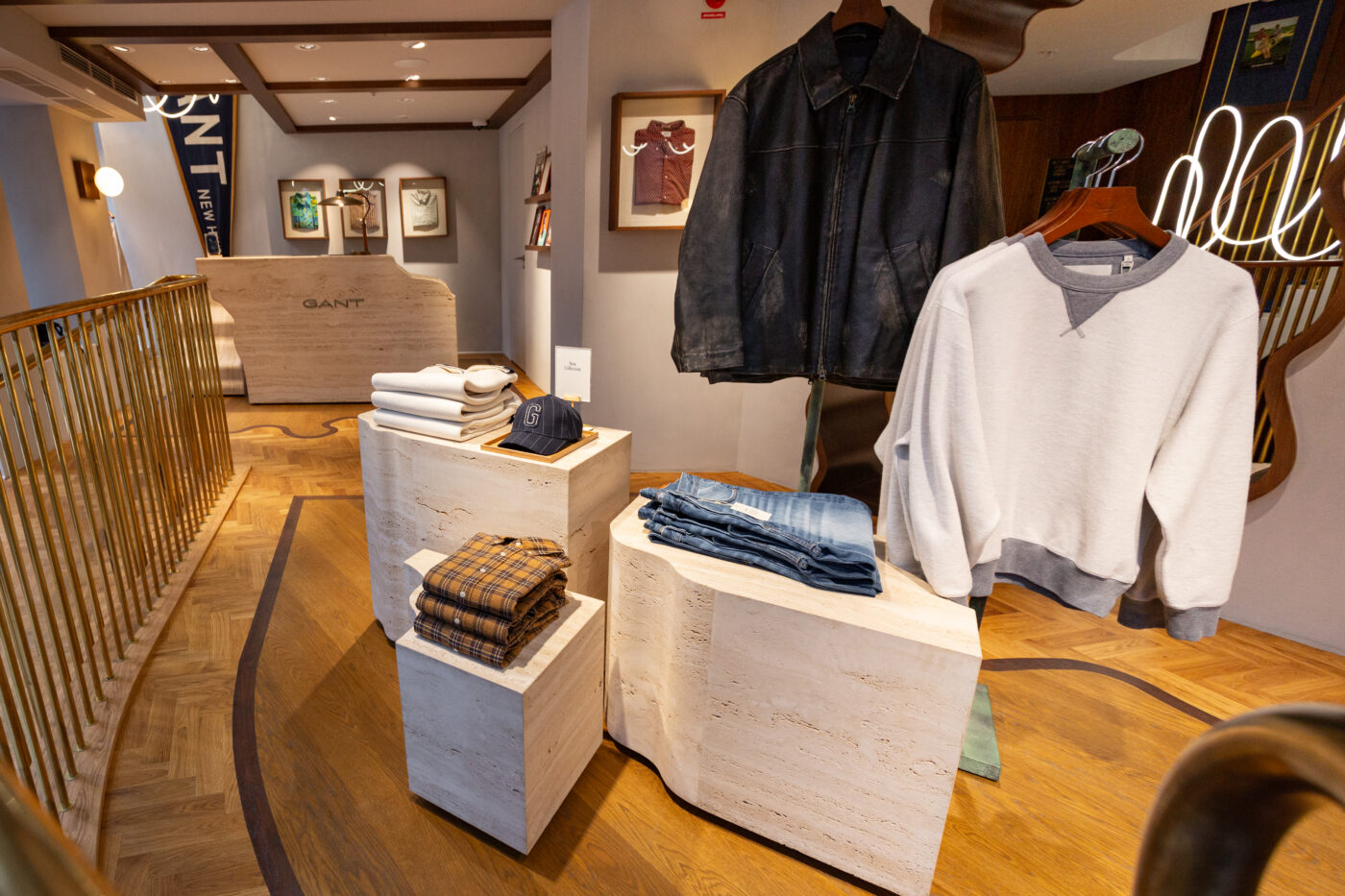 Gant Store interjöör Stockholmi näidispäevane vaade: puidust platvormid, denimjakk ja heledaks pestud hõõgu kampsun seisvas vormis ning valgustatud galerii taustal, rõhutades brändi stiili