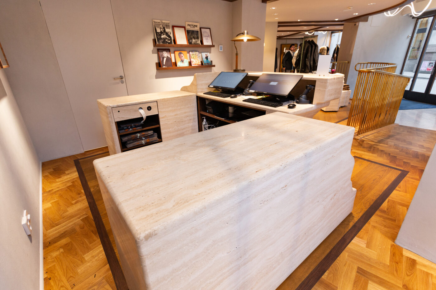 Gant Storei vastuvõtuala Stockholmi esinduslikul beigetoon marmorpõrandal, laua kohal kaks arvutit ja taustal riiulid moebrändide ajakirjadega; esiplaanil sileda pinnaga kiviaine ja kontorimööbli detailid.