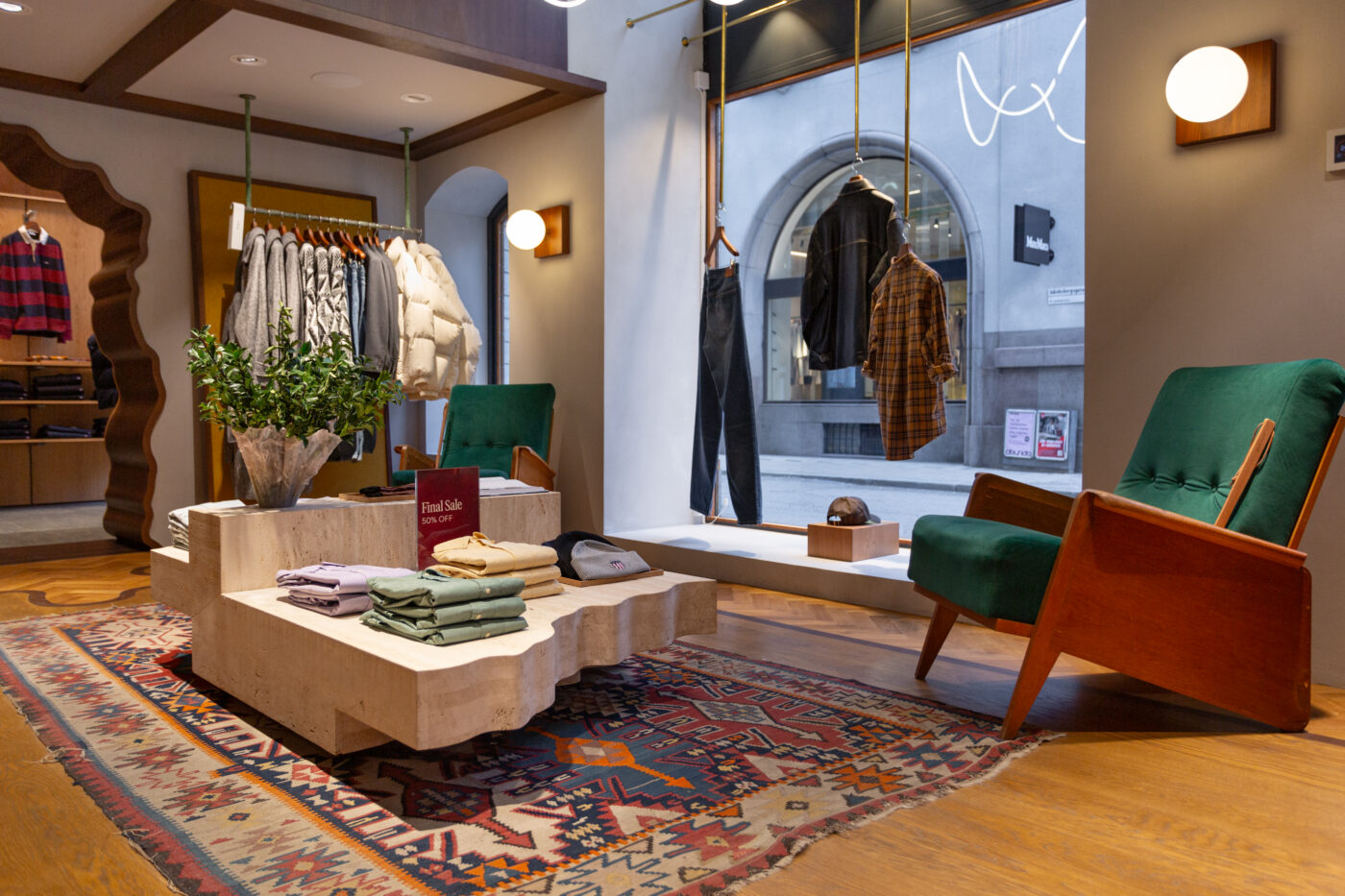 Gant Store'i sisekujundus Stockholmi vanalinna atmosfääriga, ruumis rohelised pehmed tugitoolid, puidust raamiga mööbel ja riidekardinad ning suur aknaesine näitamas välisilme.
