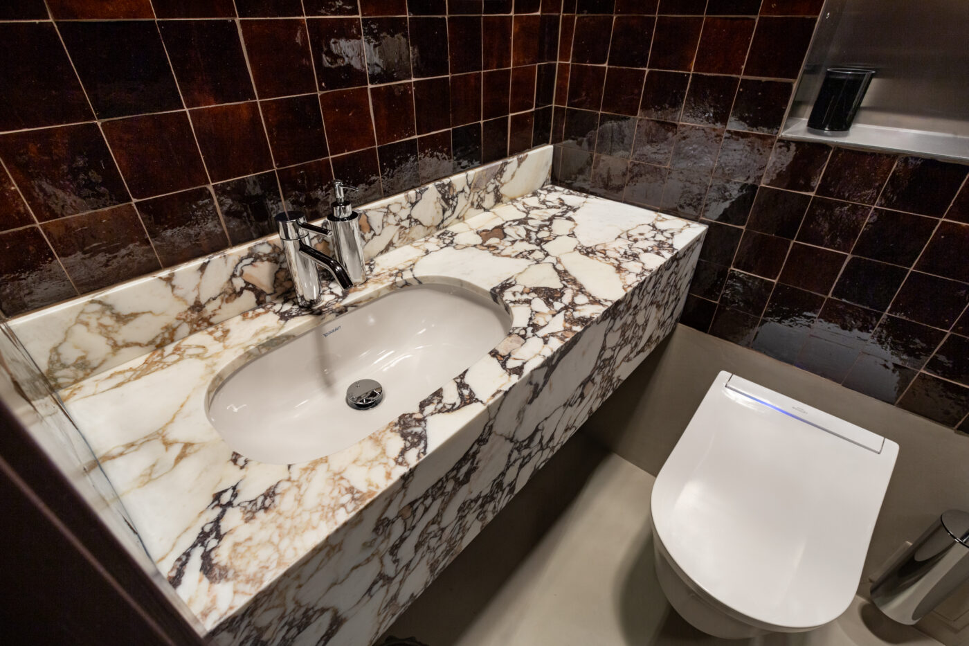 Marmorist,valge ja pruunide mustritega vannitoa countertops ja vahendustega segistid ning neutraalsed pruunid seinad; projekt Apartment Max by Marmi Futerno, Estonia