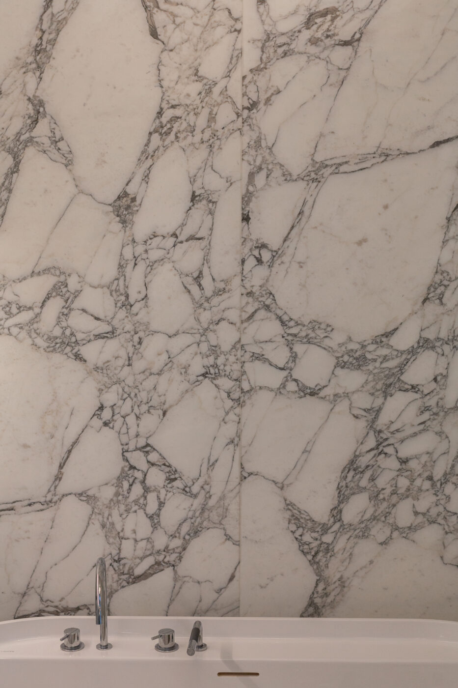 Apartment Callans projektist - valge marmormusteri sein, hallide veenidega peen lõiked, vannitoa valge bassein ja roostevabast terasest faucet.