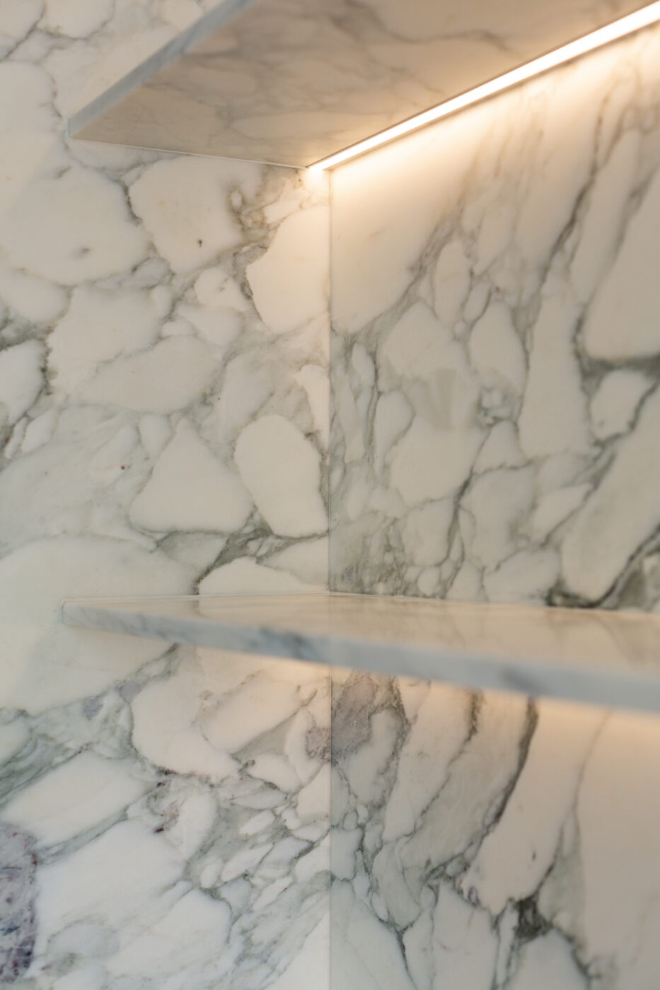 Valge marmormööbli külg ja riiulid peene hallide veenidega muster, pehmed soojad valgustid ja rafineeritud pinna detailid; projekt Apartment Callans, Marmi Futerno