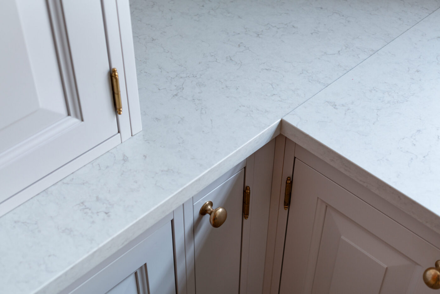 White marble countertop with subtle gray veining in a clean kitchen setting, featured in Apartment Leon by Marmi Futerno, showcasing light cabinetry and brass hardware.