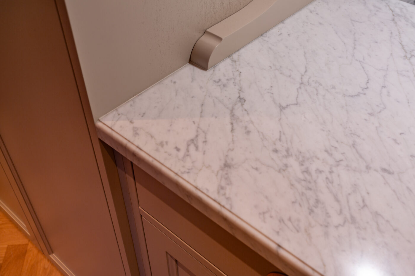 Valge marmorkas countertop köögis ümbritsetud hallide kappide ja beige seintega; nähtav on peen marmorvood, mille hallid veenid annavad tekstuuri.