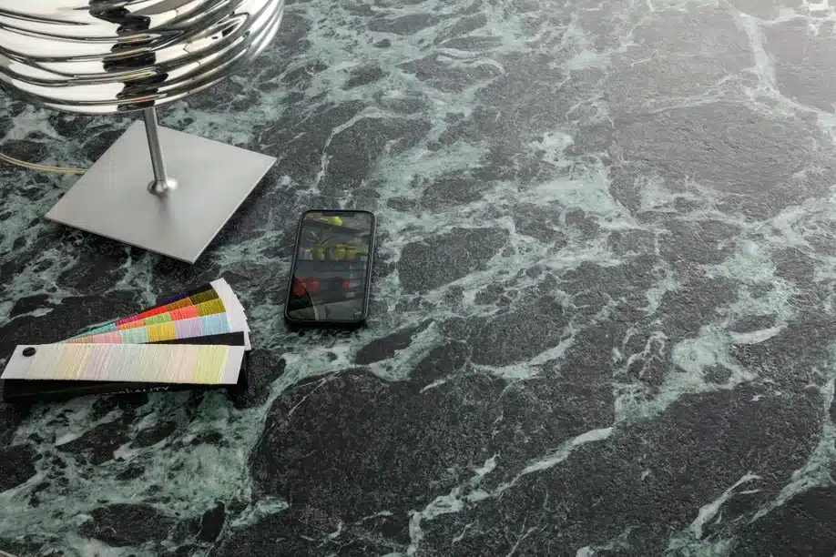 Verde Alpi marble surface with a lamp, color swatches, and a phone displaying a shelf of items.