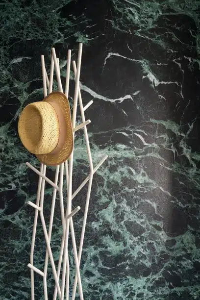 Straw hat on a white coat rack against Verde Alpi marble wall.