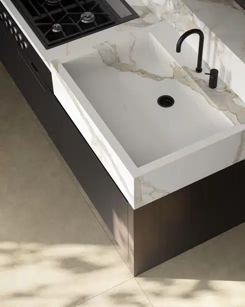 Calacatta Michelangelo marble countertop with a modern sink and black faucet, next to a cooktop.