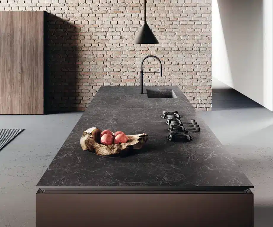 Nero Greco kitchen island with dark countertop, sink, stove, and fruit bowl against a brick wall.