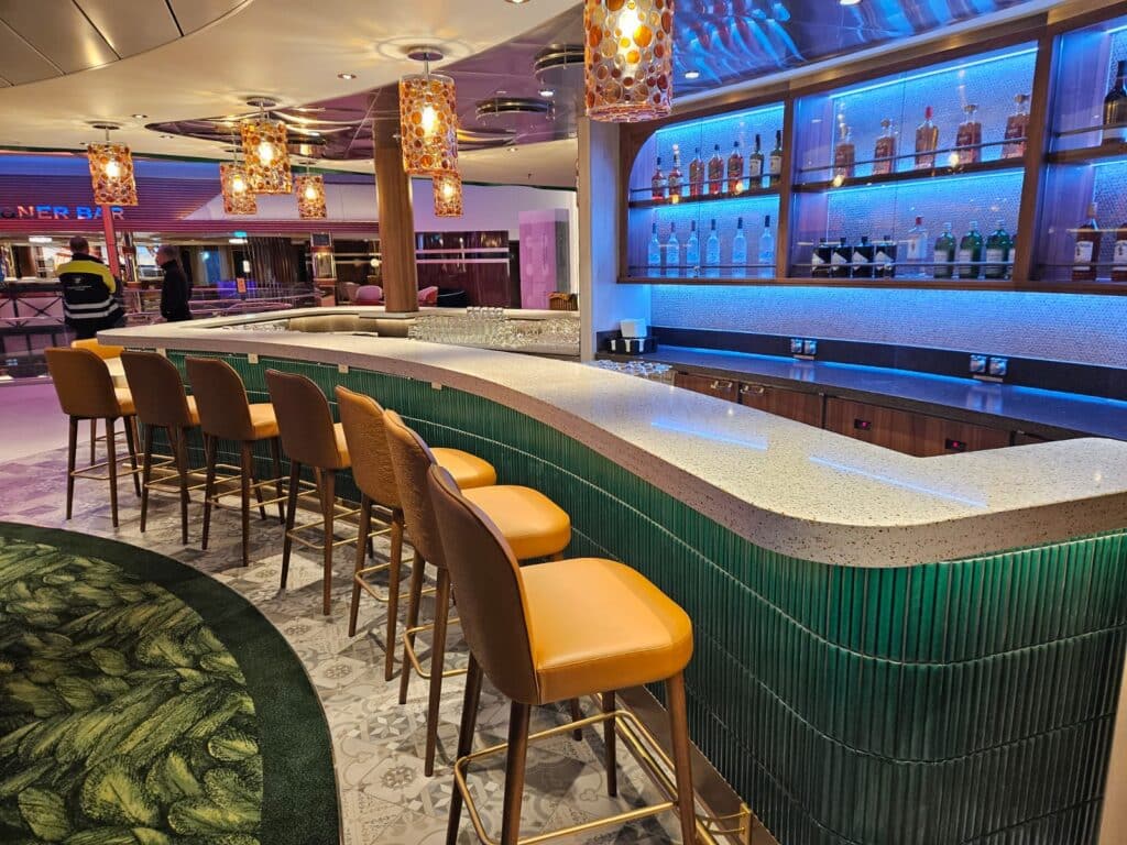 Speckled stone bar counter with blue backlighting, glowing pendant lights, and neatly arranged bottles inside a cruise yacht bar area.