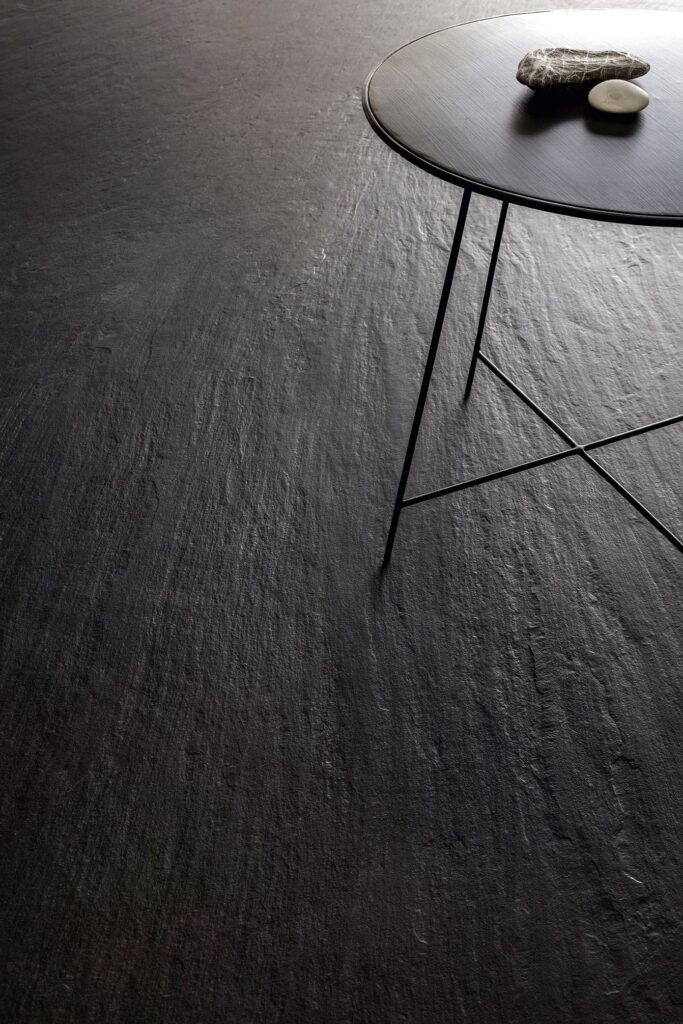 Dark textured floor with a small black table and two stones. Laminam Ardesia Nero.
