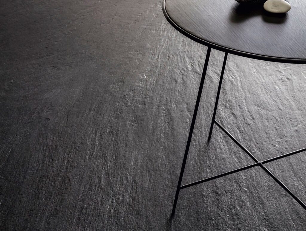 Dark textured floor with a small black table and two stones. Laminam Ardesia Nero.