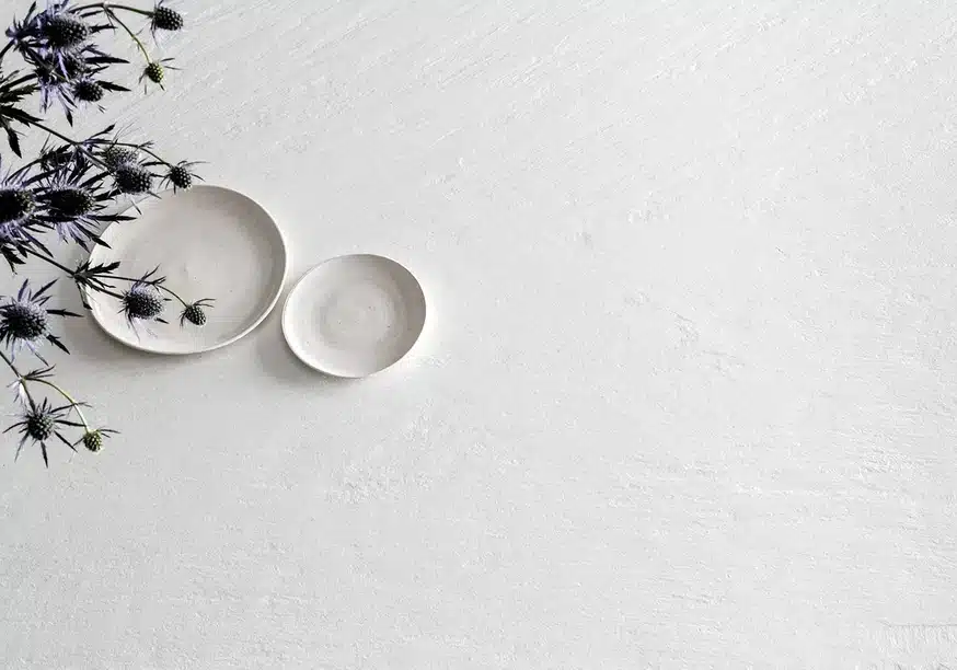 Laminam Ardesia Bianco: Two white plates and thistle flowers on a textured white surface.