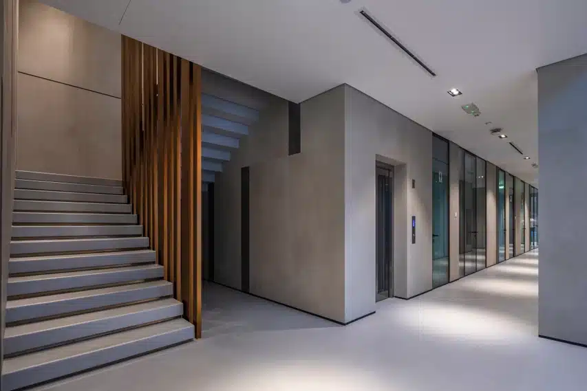Calce Antracite Laminam hallide toonidega koridor - vasakul tumedavõitu trepikoda ja paremal klaasustud uksed, kaasaegne arhitektuur ja tekstuuride kontrast