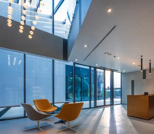 Moderne interjöör Laminam Calce Antracite tooniga, avatud klaasist seinad, minimalistlikud kollase-oranžid lounge-toolid ja pehme valgus.