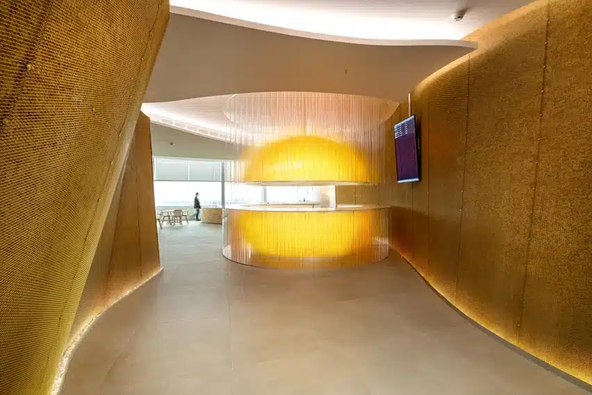 Laminam Calce Grigio viimistlusega interjöör, kuldse tooniga seinapaneelid ning kesksel kergelt kumav ümmargune valgustusega baar/koosolekuala