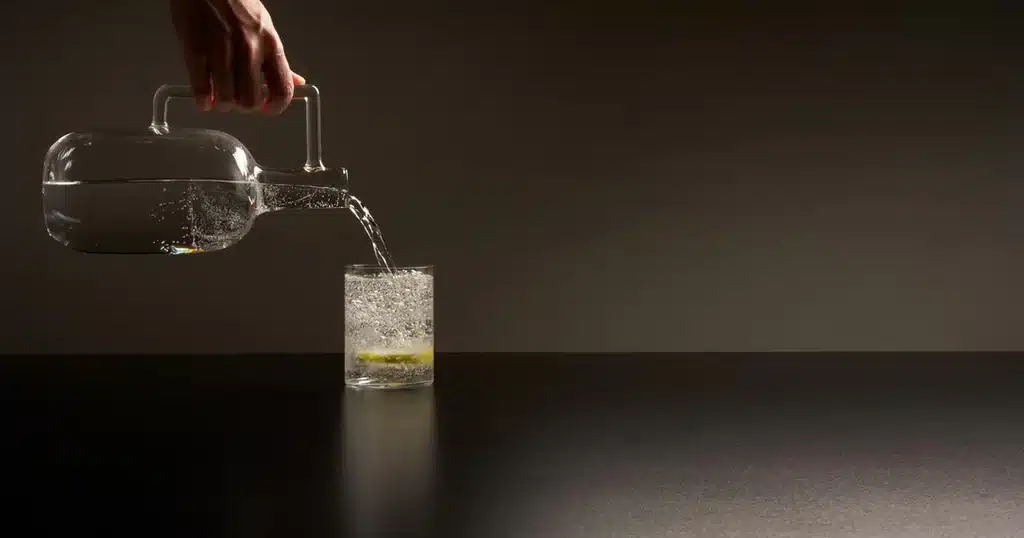 Water being poured from a glass carafe into a glass with lemon, on Laminam Nero Assoluto surface.