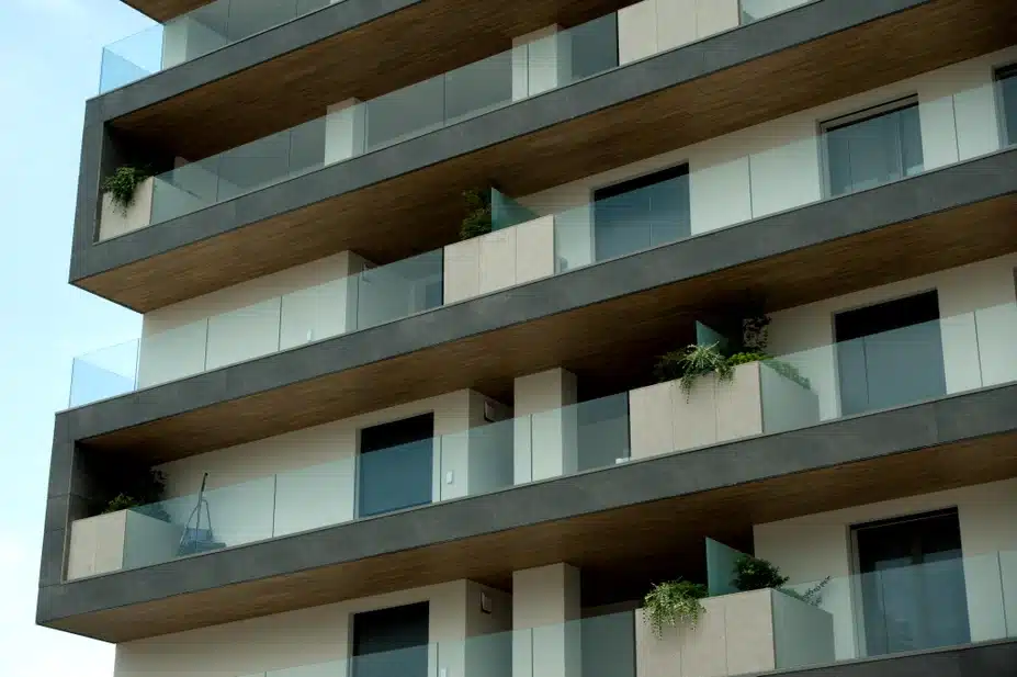 Laminam Piombo Fokos toodega seotud plaatide tekstuur näidatud moodsas korterelamus, hall-beige toonid, klaasbalustraadid ning rohelised taimed korruste vahel.