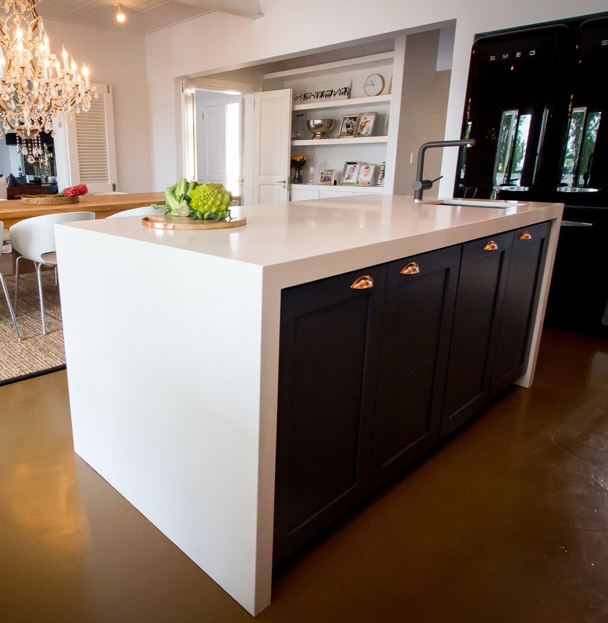 Caesarstone 5141 Frosty Carrina quartz tops a modern kitchen island with black cabinetry, a matte black faucet, and a glossy Smeg fridge.