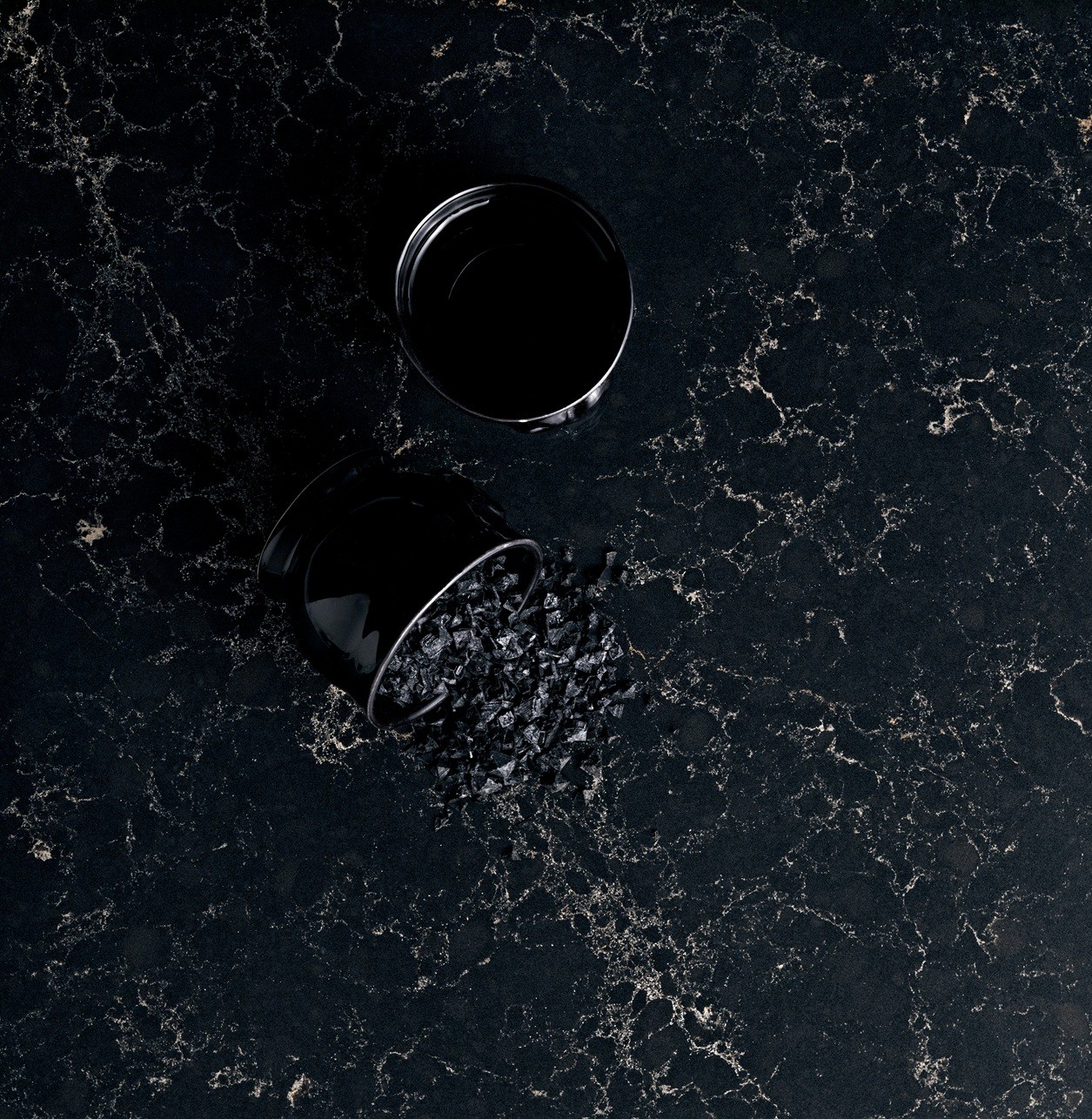 Black quartz countertop with spilled dark salt crystals and a black container.